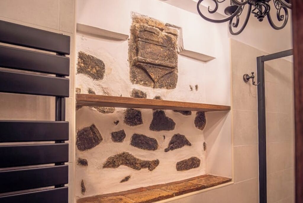 Un baño con pared de piedra, estante de madera y lámpara de metal negro.