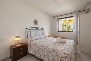 Een slaapkamer met een bed, bedlampen, een nachtkastje, een raam met gordijnen en een wandairconditioner.