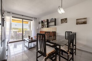 Een eetgedeelte met een glazen tafel en stoelen, een bank, een boekenkast en een stadsgezichtschilderij aan de muur.