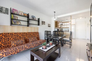 Een moderne woonkamer met een gestreept bankje, een salontafel met potplanten, een eethoek met stoelen, en een keuken die door een open deur zichtbaar is.