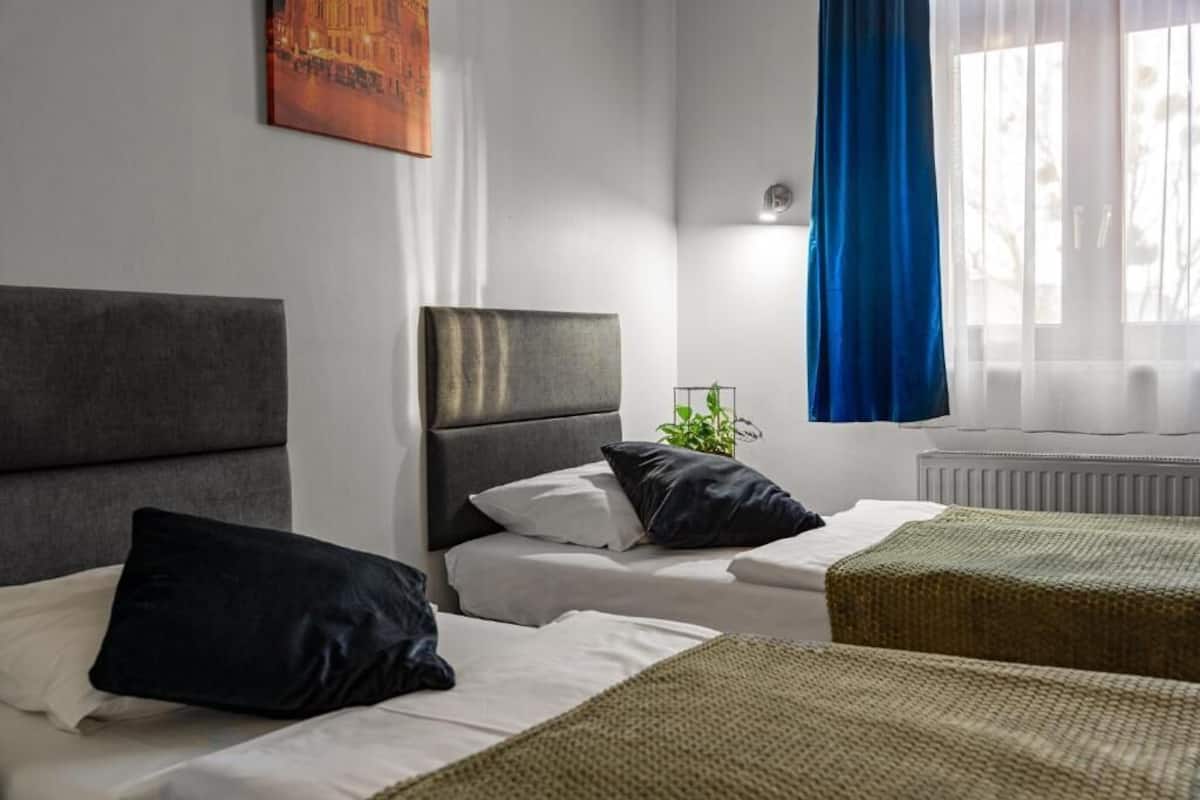 A hotel room with two beds, a large window with blue curtains, and a radiator.