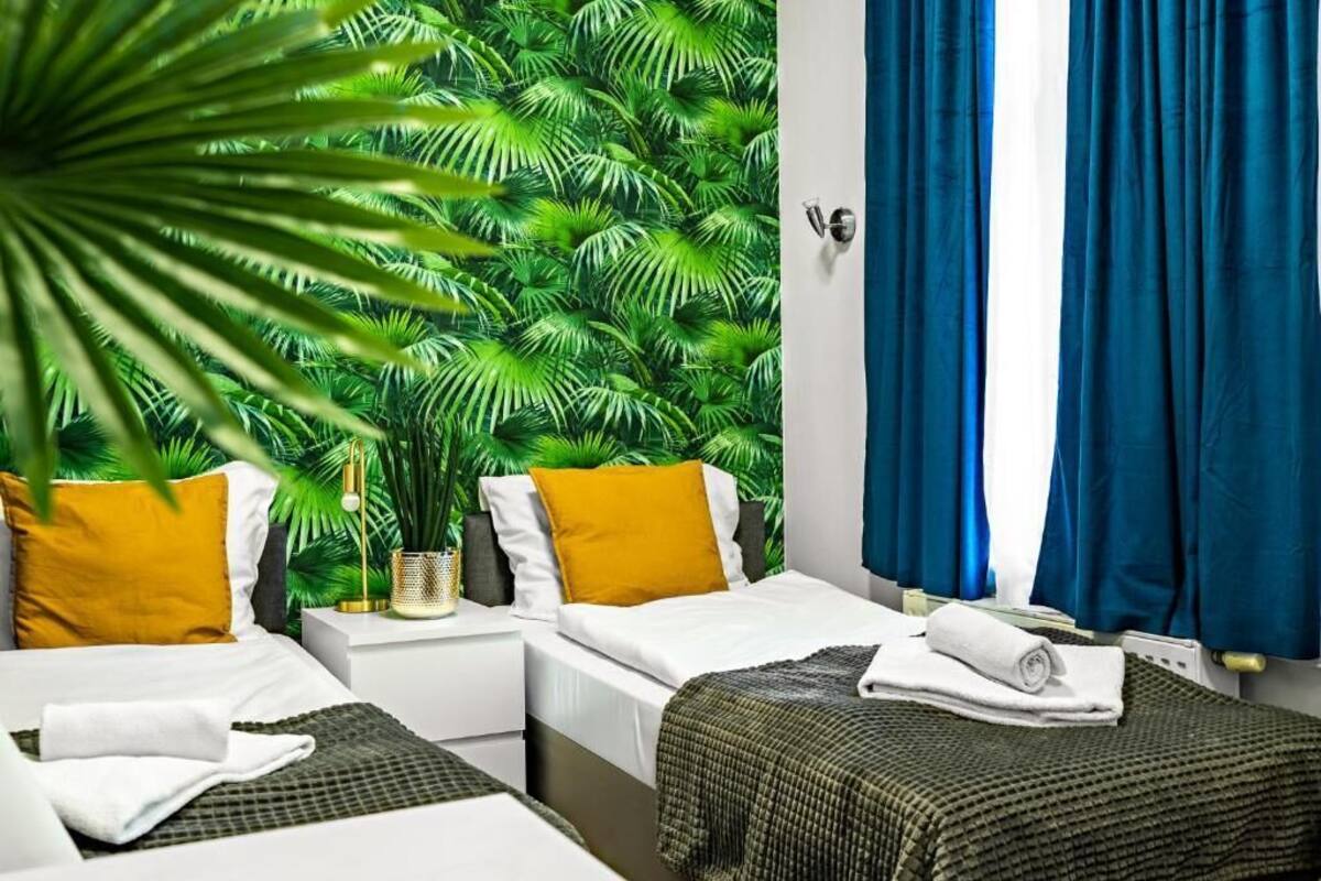 A hotel room with two beds, a large potted plant, and a wall with a tropical leaf pattern.