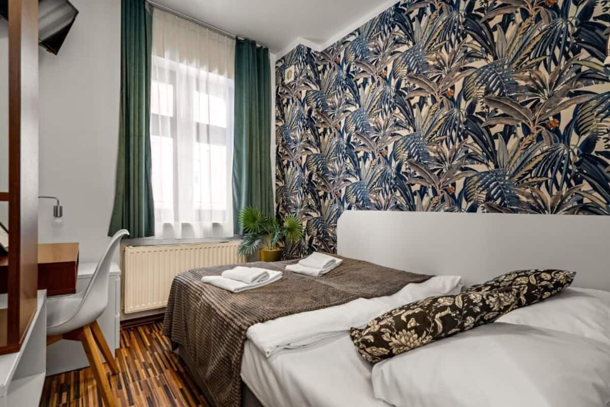 A hotel room with a bed, a desk, and a window with curtains.