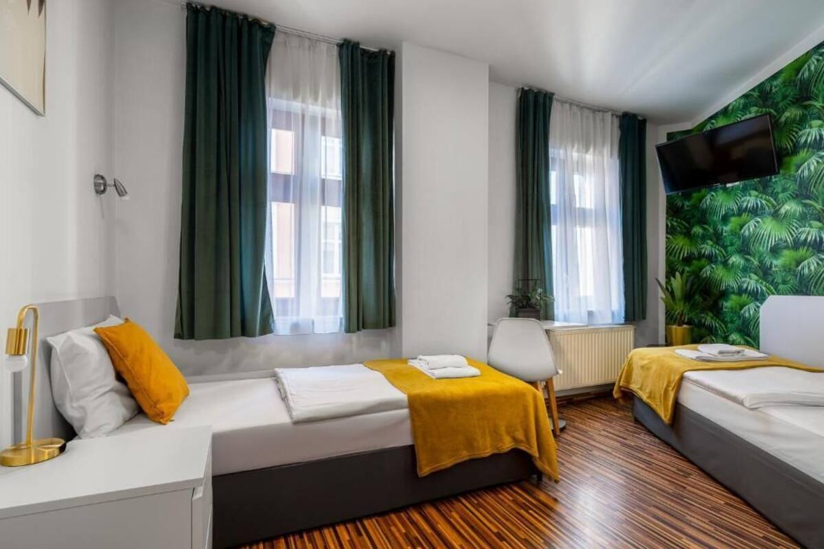 A hotel room with two beds, a TV mounted on the wall, and a large window with curtains.
