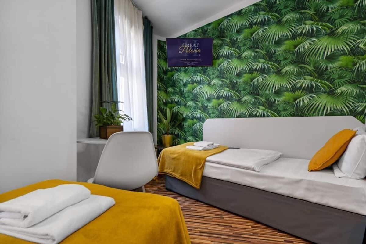 A hotel room with a bed, a sofa, a small table with a yellow tablecloth, and a wall with a tropical leaf pattern.