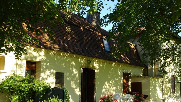 A house with a brick roof, a front door, and a small porch with white chairs and potted plants. - Gîte de Peyregras Villereal (Rives)