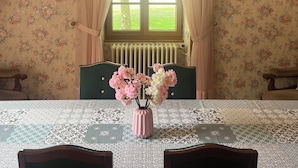 A dining area with a table set for four, a vase of flowers, and a window with curtains. - Gîte de Peyregras Villereal (Rives)
