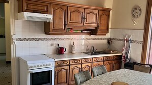 A kitchen with wooden cabinets, a white stove, and a dining table with chairs. - Gîte de Peyregras Villereal (Rives)