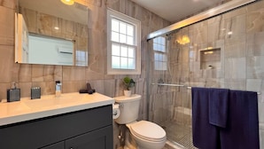 Een moderne badkamer met een douchecabine van glas, een wit toilet en een wastafel met spiegel.