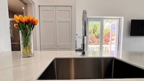 Een moderne keuken met een roestvrijstalen spoelbak, een bloevas op het aanrecht en uitzicht op een balkon met een balustrade.