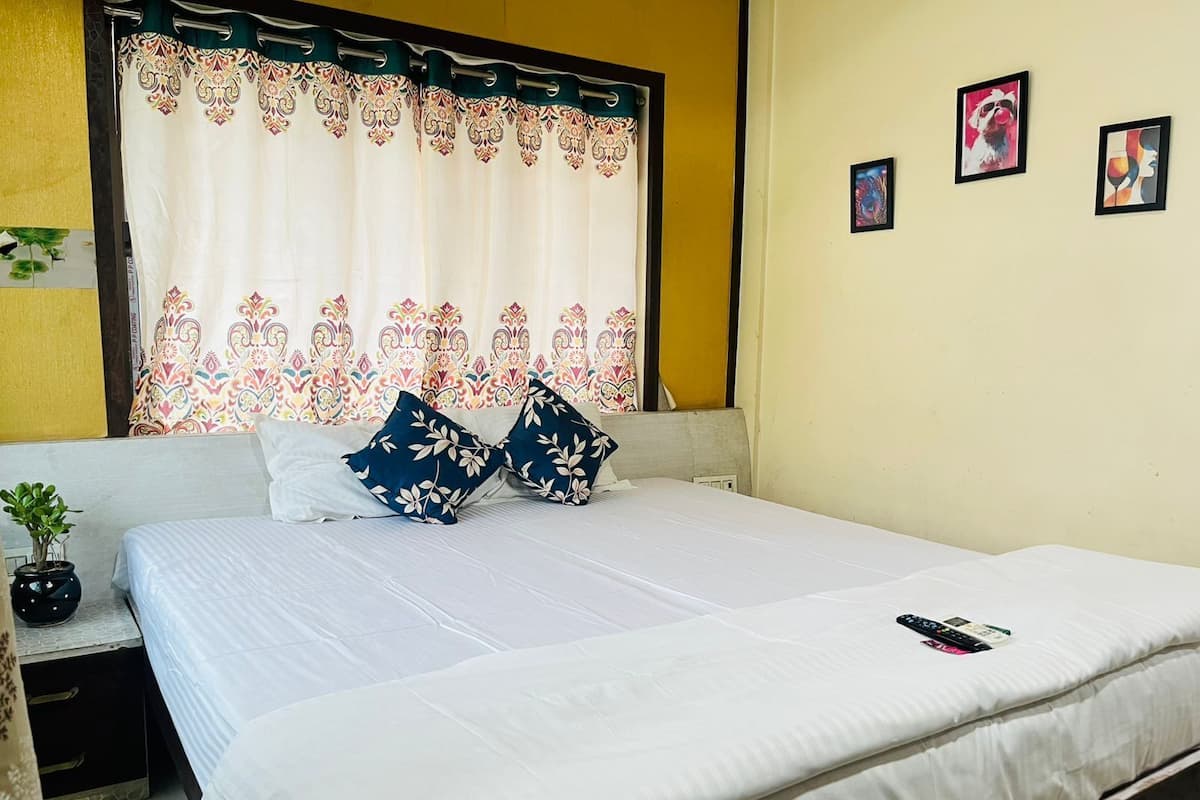 A neatly made bed with white bedding and two decorative pillows, a small bedside plant, and a remote control on the bed.