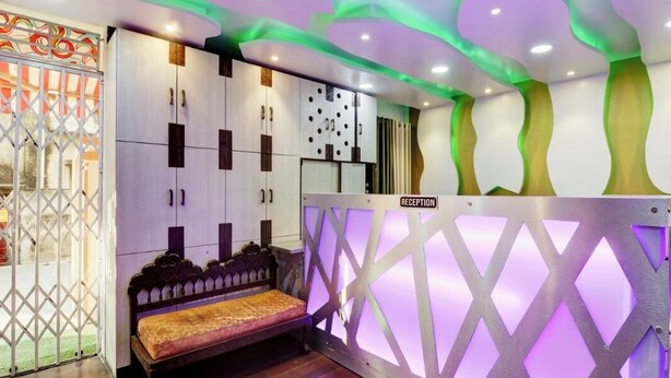A reception area with a bench, a reception desk, and a decorative wall with a 'RECEPTION' sign. - Green Edge Regency (Kolkata)