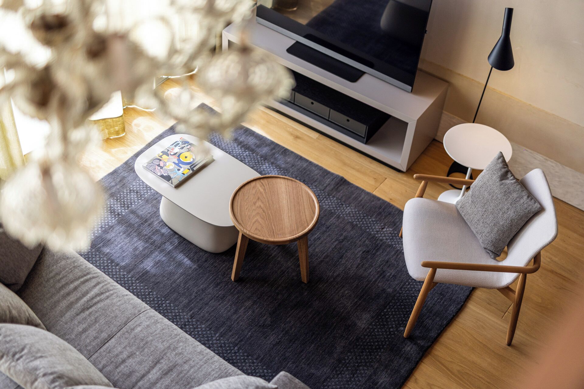 A modern living room with a sofa, a round coffee table, a chair with a cushion, a flat-screen TV, and a lamp.