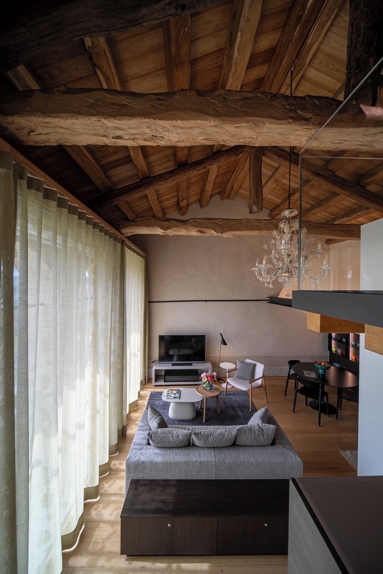 Una sala de estar moderna con techo de madera, un televisor grande, un sofá y un comedor.
