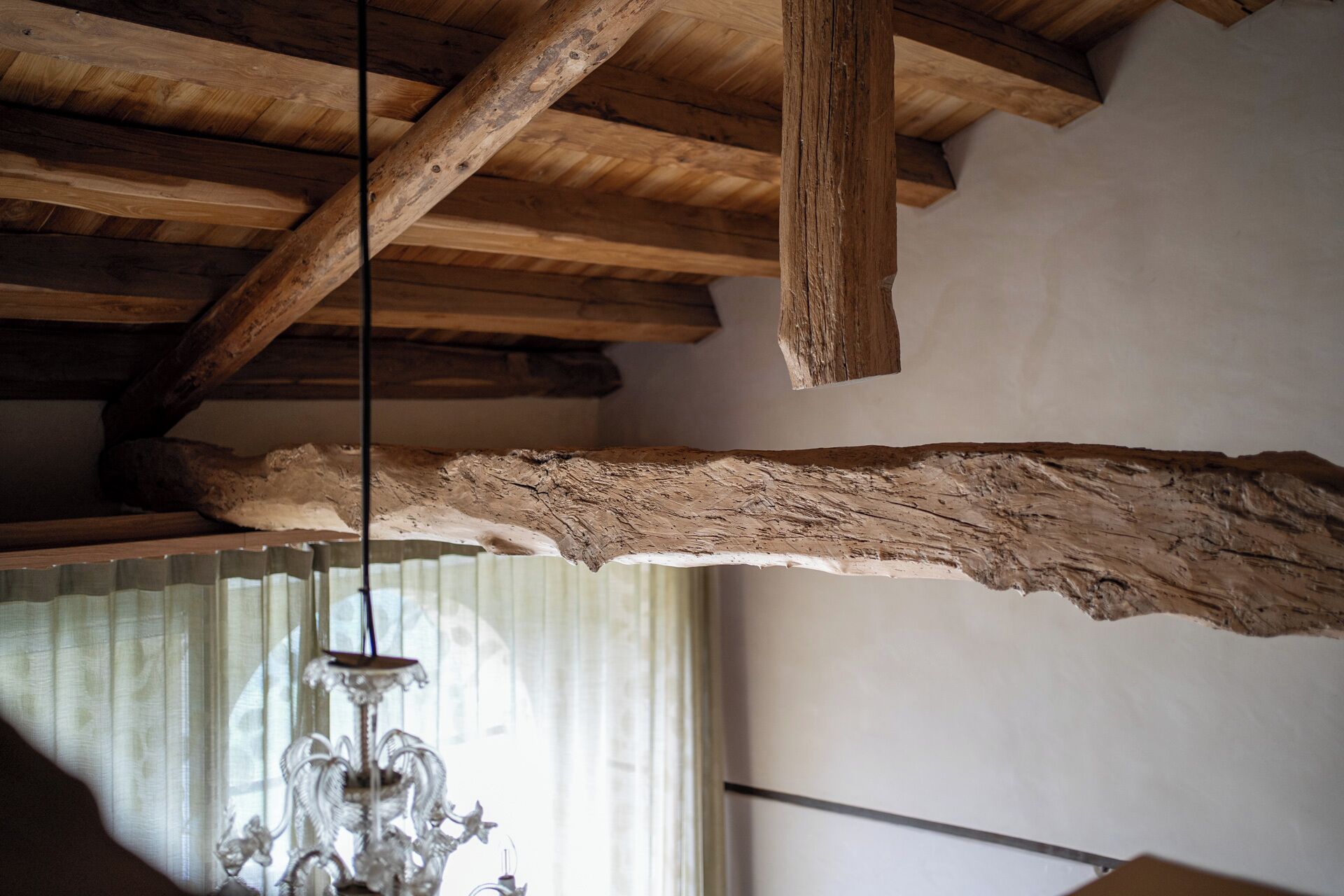 Techo de madera con vigas a la vista y una viga grande de textura rugosa colgando.