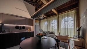 A modern kitchen with a central island, a dining area with a round table, and a living room with a sofa and large windows. - Tenuta Duchi Corbanus (Tarzo)