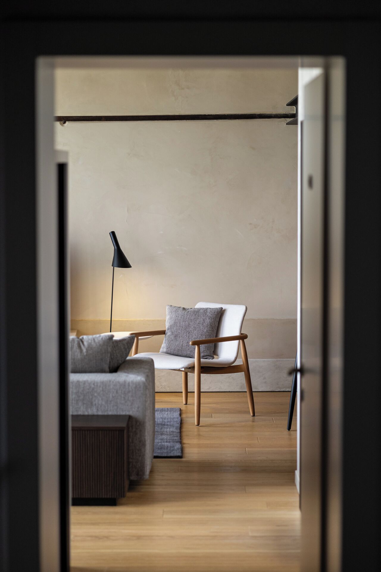 A modern living room with a sofa, a chair, a floor lamp, and a view through an open door.