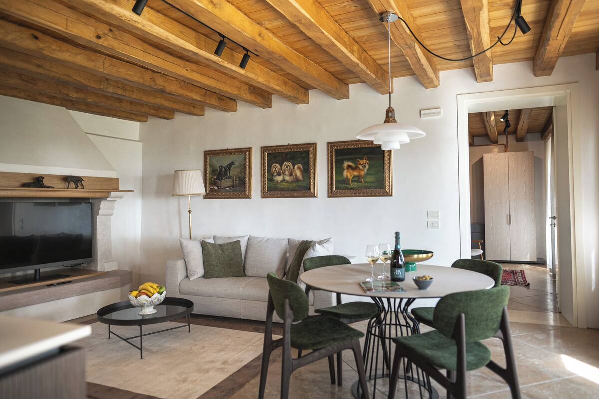 A living room with a sofa, a dining table with chairs, a TV, and artwork on the wall.