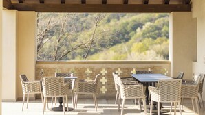 An outdoor patio with a wooden ceiling, a stone wall with a cross pattern, and a view of trees and hills. - Tenuta Duchi Corbanus (Tarzo)