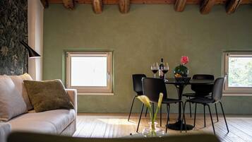 A cozy room with a wooden ceiling, a sofa with cushions, a dining table with chairs, and a window with a view.