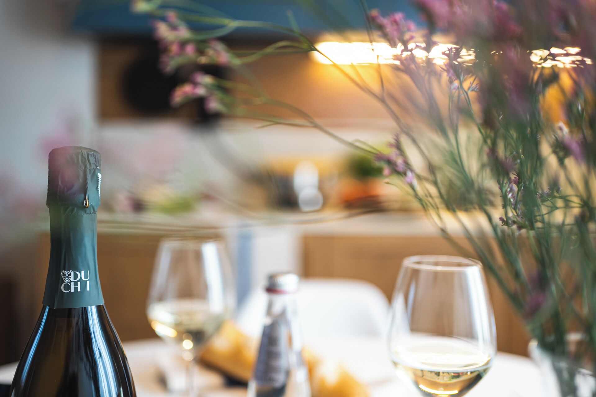 A bottle of Du Chi wine, a glass of white wine, and a vase with flowers on a table.