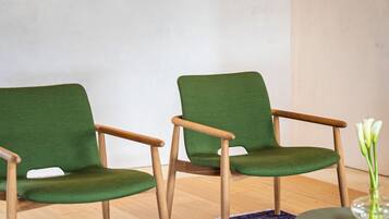 Una habitación con dos sillones tapizados en verde, una mesita redonda con limones y un jarrón con flores sobre una pequeña mesa.