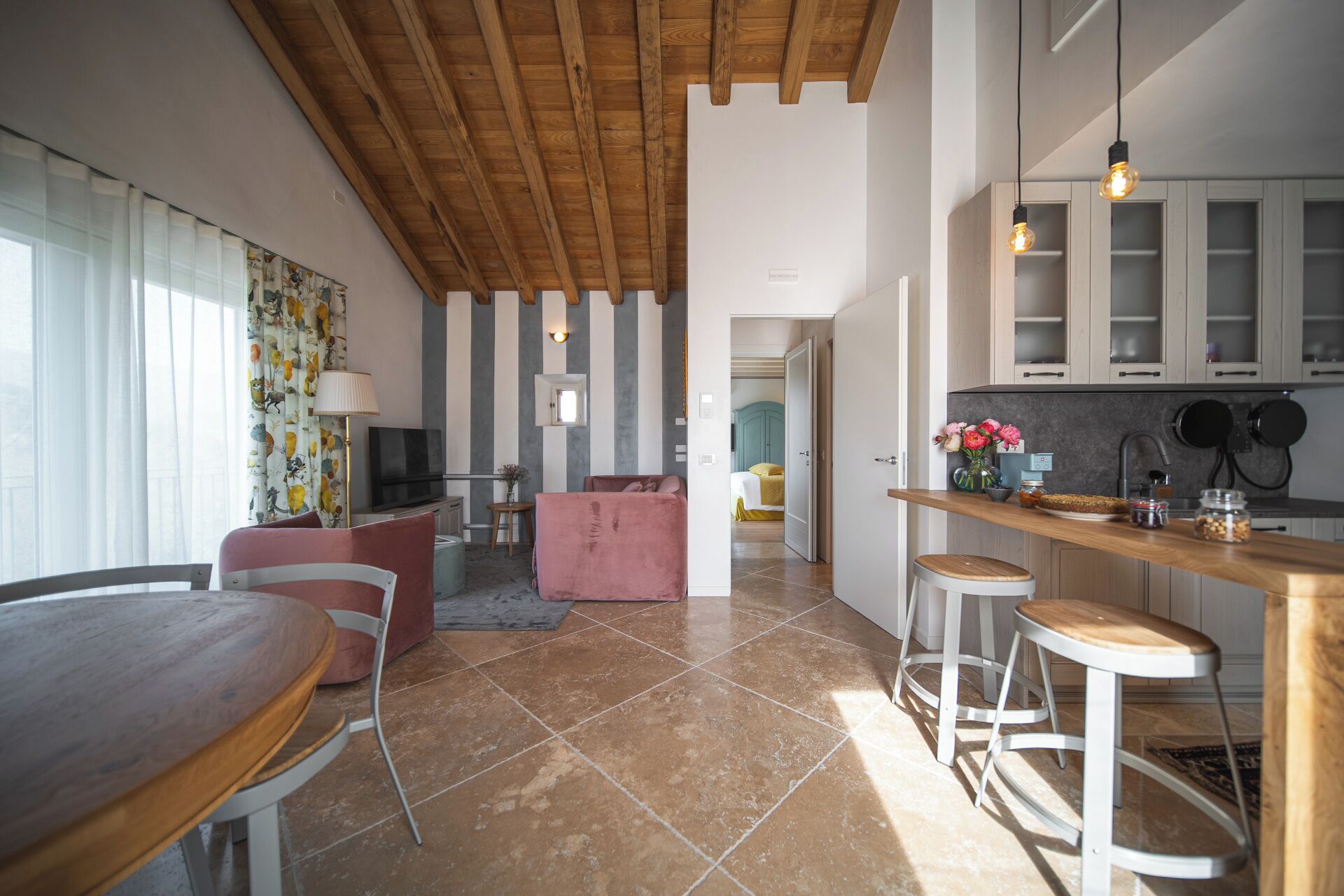 Eine moderne Küche mit Holzausstattung, ein Essbereich mit Holztisch und -stühlen sowie ein Wohnzimmer mit rosa Sofa und Fernseher.