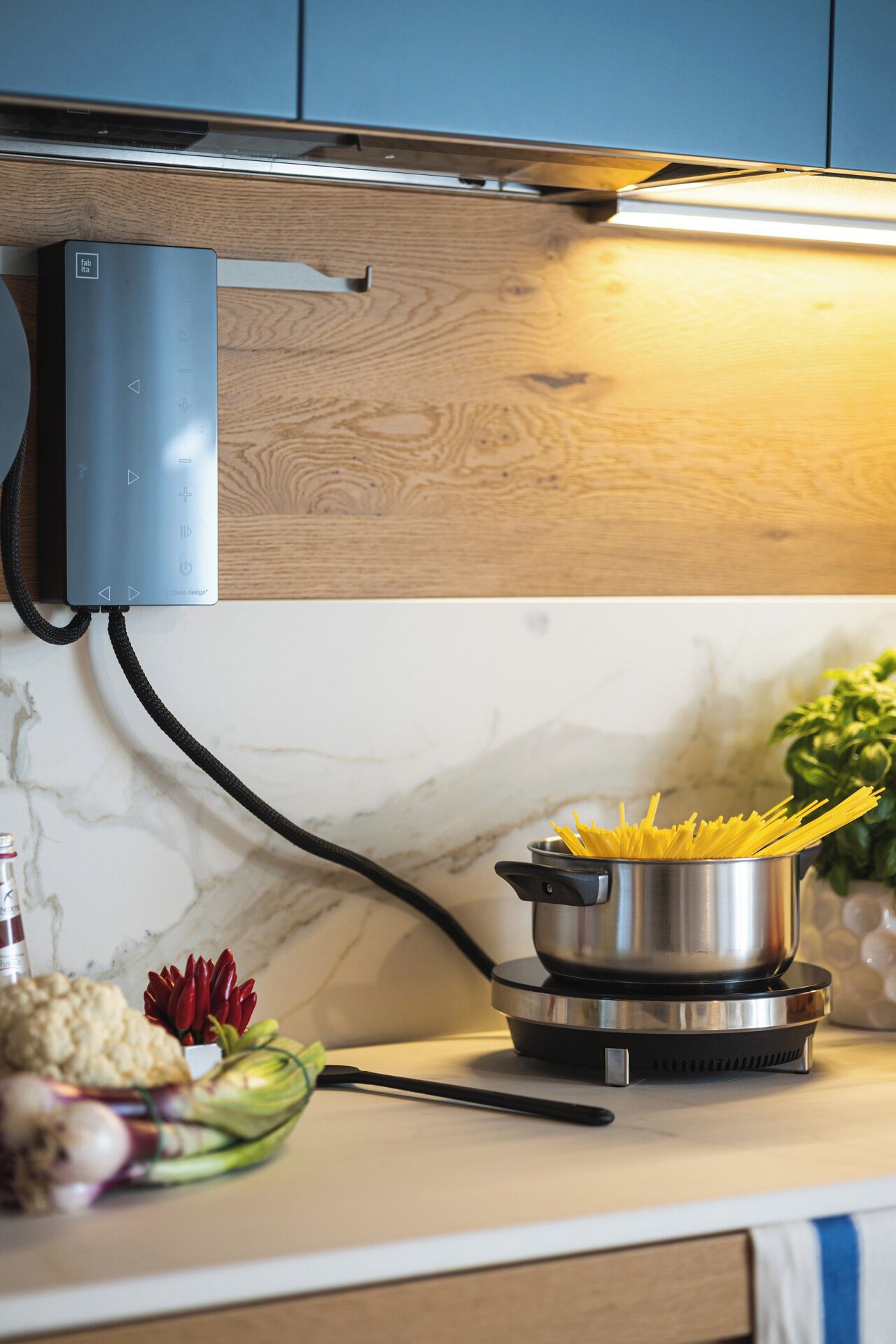 A kitchen with a modern stove, a pot of spaghetti, and fresh vegetables on the counter.