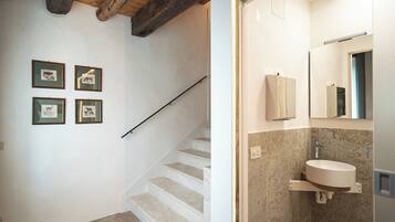A staircase leading to a bathroom with a sink and mirror, wooden beams on the ceiling, and a patterned rug on the floor.