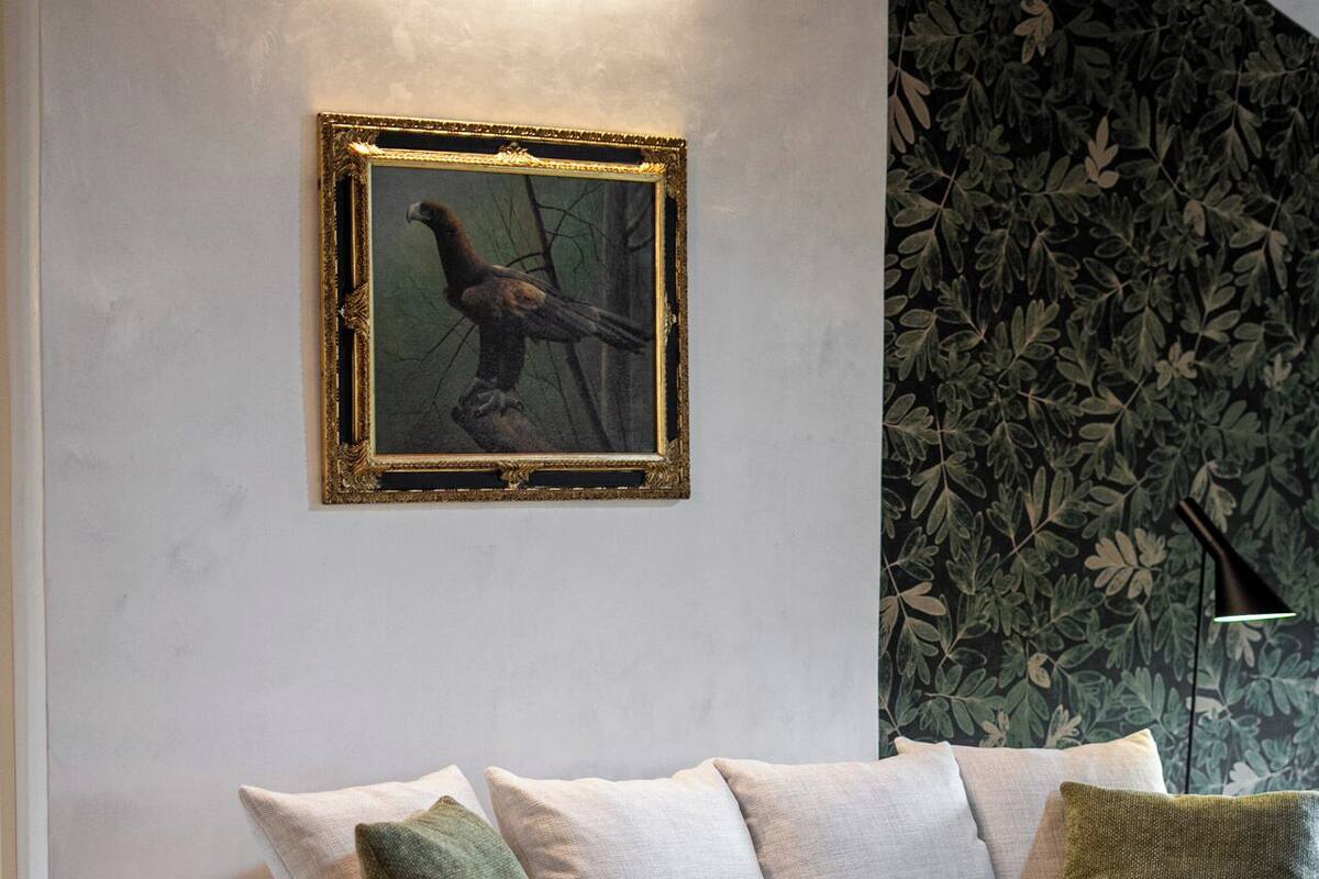 A modern living room with a grey sofa, green chairs, a small table with a vase, and a framed picture on the wall.
