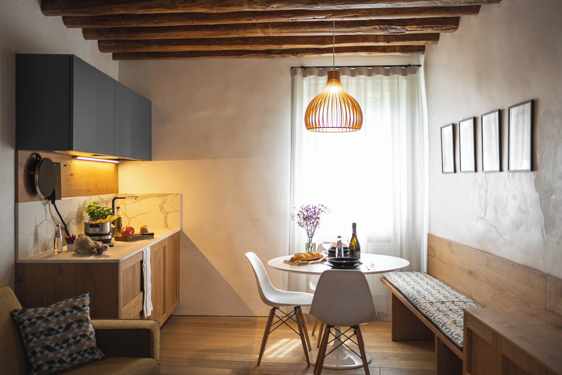 A compact kitchen with a built-in stove, a dining area with a round table and chairs, and a bench.