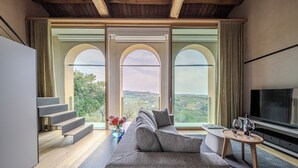 A modern living room with a large sofa, a TV, and a view of the countryside through arched windows. - Tenuta Duchi Corbanus (Tarzo)