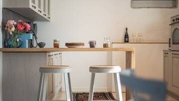A kitchen with a wooden countertop, two white stools, a vase with flowers, and jars of food.