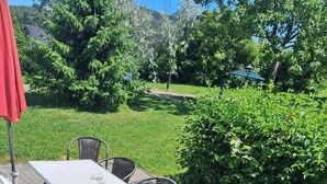 An outdoor patio area with a table and chairs, surrounded by greenery and a pathway. - Cozy bungalow in the heart of the Eichsfeld (Uder)