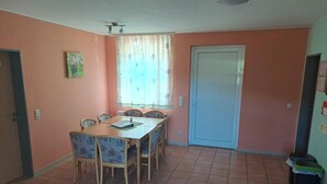 A dining area with a wooden table and chairs, a window with curtains, a closed door, and a tiled floor. - Cozy bungalow in the heart of the Eichsfeld (Uder)