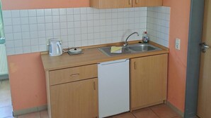 A compact kitchen with wooden cabinets, a white dishwasher, and a tiled backsplash. - Cozy bungalow in the heart of the Eichsfeld (Uder)