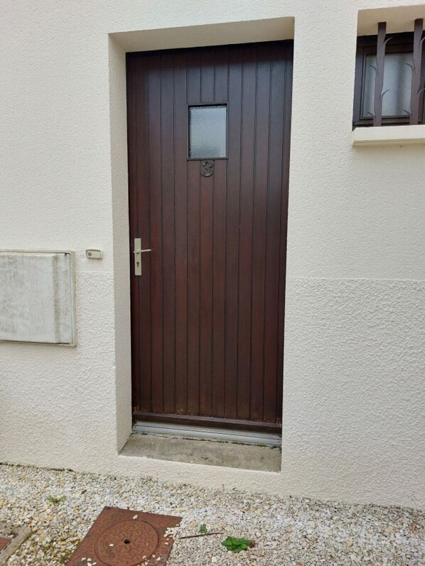 A dark wooden door with a small window above it, set in a white wall.
