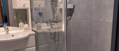 Un baño moderno con ducha de vidrio, tocador blanco con espejo y suelo de baldosas.