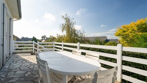 A patio with a round table and chairs, a white fence, and a view of trees and buildings. - Holiday Home 'Maison De Caractère' with Shared Terrace, Private Garden and Wi-Fi (Cancale)