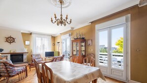 A dining area with a table, chairs, and a chandelier. There is a fireplace, a television, and a ship model on the wall. - Holiday Home 'Maison De Caractère' with Shared Terrace, Private Garden and Wi-Fi (Cancale)