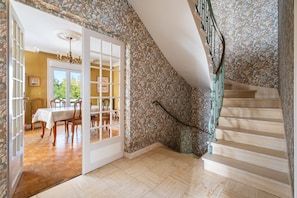 A staircase with a floral wallpaper, a dining area with a table and chairs, and a chandelier.