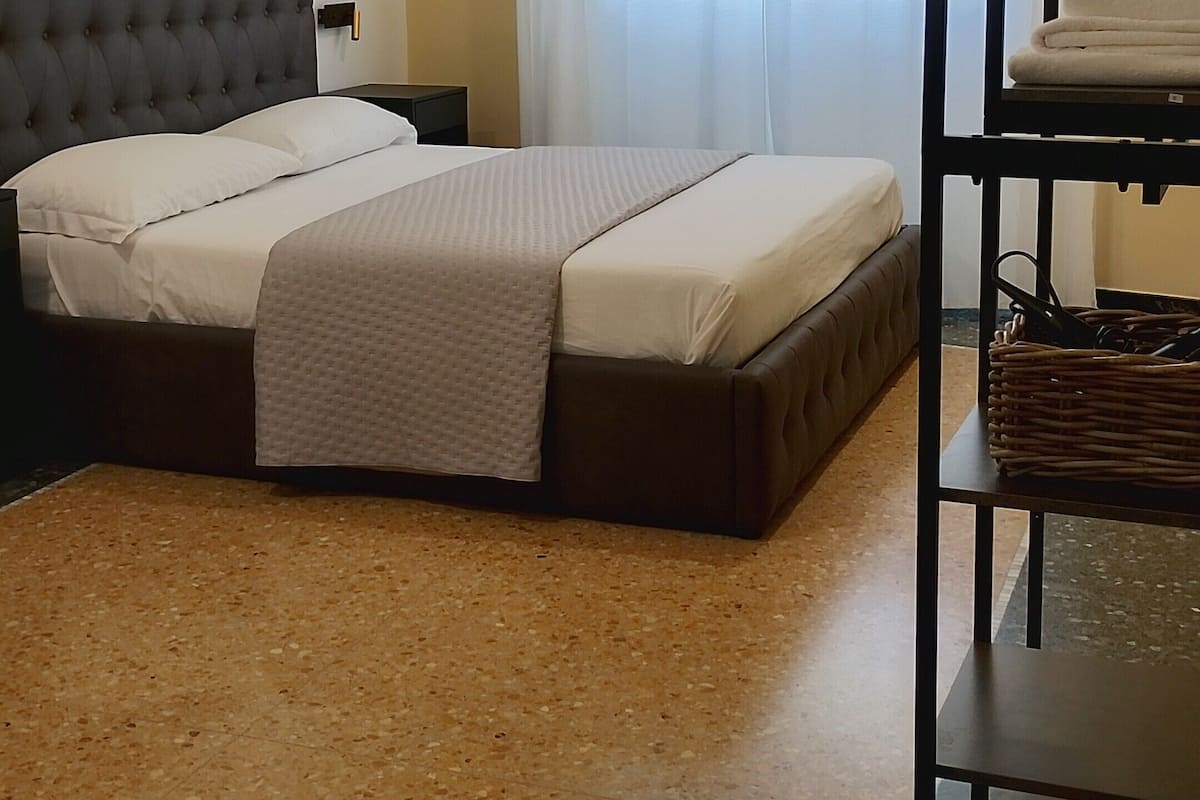Un dormitorio ordenado con una cama, una mesita y un estante con objetos colgados.
