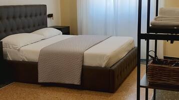 Un dormitorio ordenado con una cama, una mesita y un estante con objetos colgados.