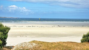 A beach with a sandy shore, a grassy area in the foreground, and a lighthouse in the distance. - Ker Aloueder, sleeps 10, beach access, panoramic sea view (Santec)