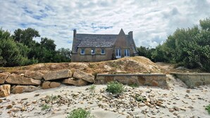 A stone house with a steep roof, surrounded by a rocky landscape and dense foliage. - Ker Aloueder, sleeps 10, beach access, panoramic sea view (Santec)