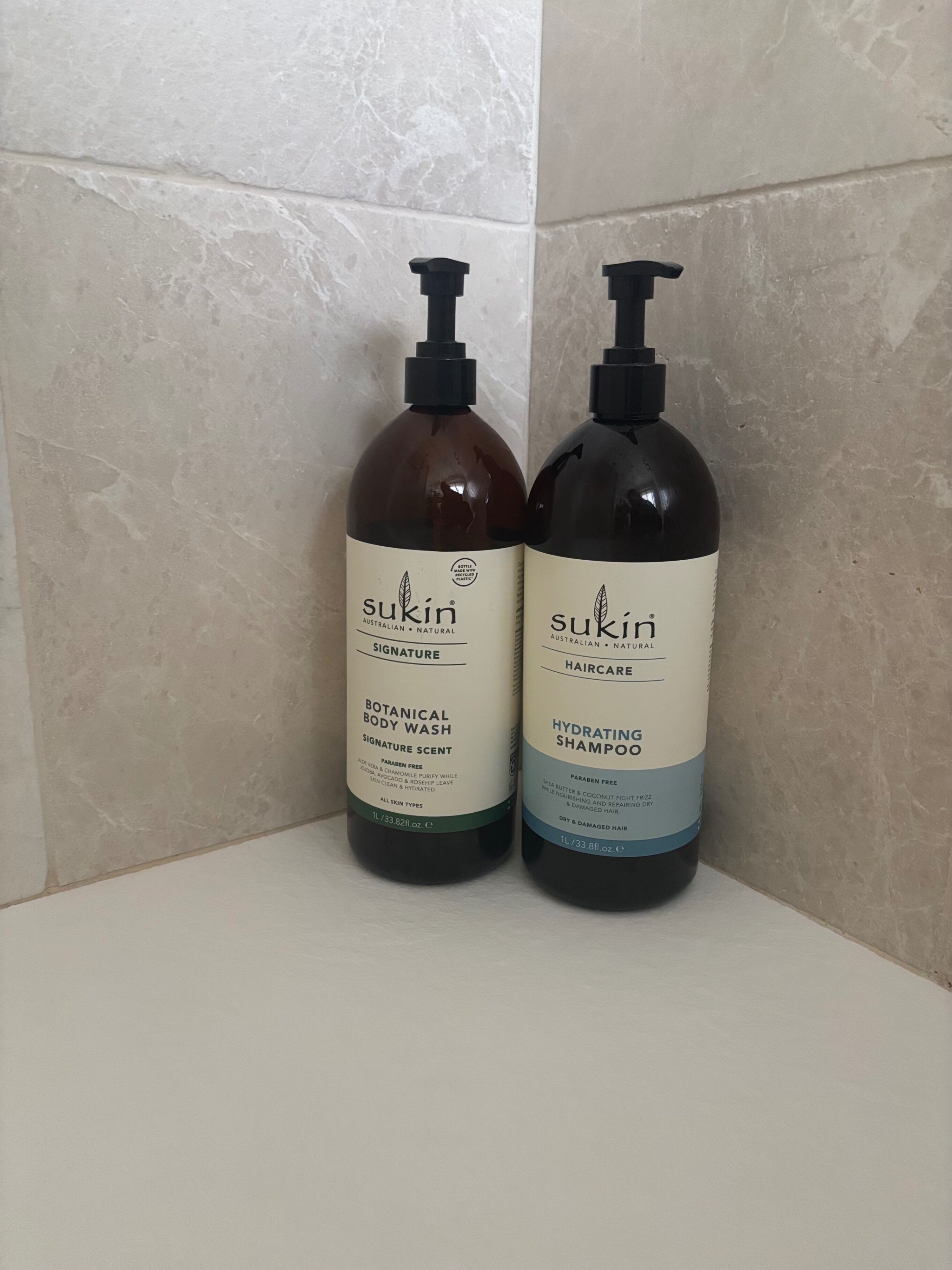 Two bottles of Sukun haircare products on a white surface against a tiled wall.