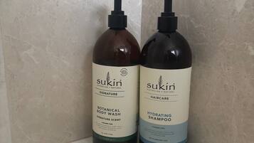 Two bottles of Sukun haircare products on a white surface against a tiled wall.