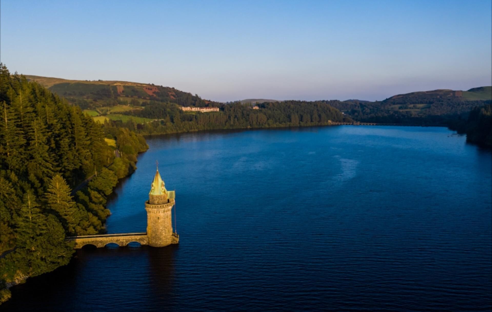 Ein Turm an einem See, umgeben von bewaldeten Hügeln.