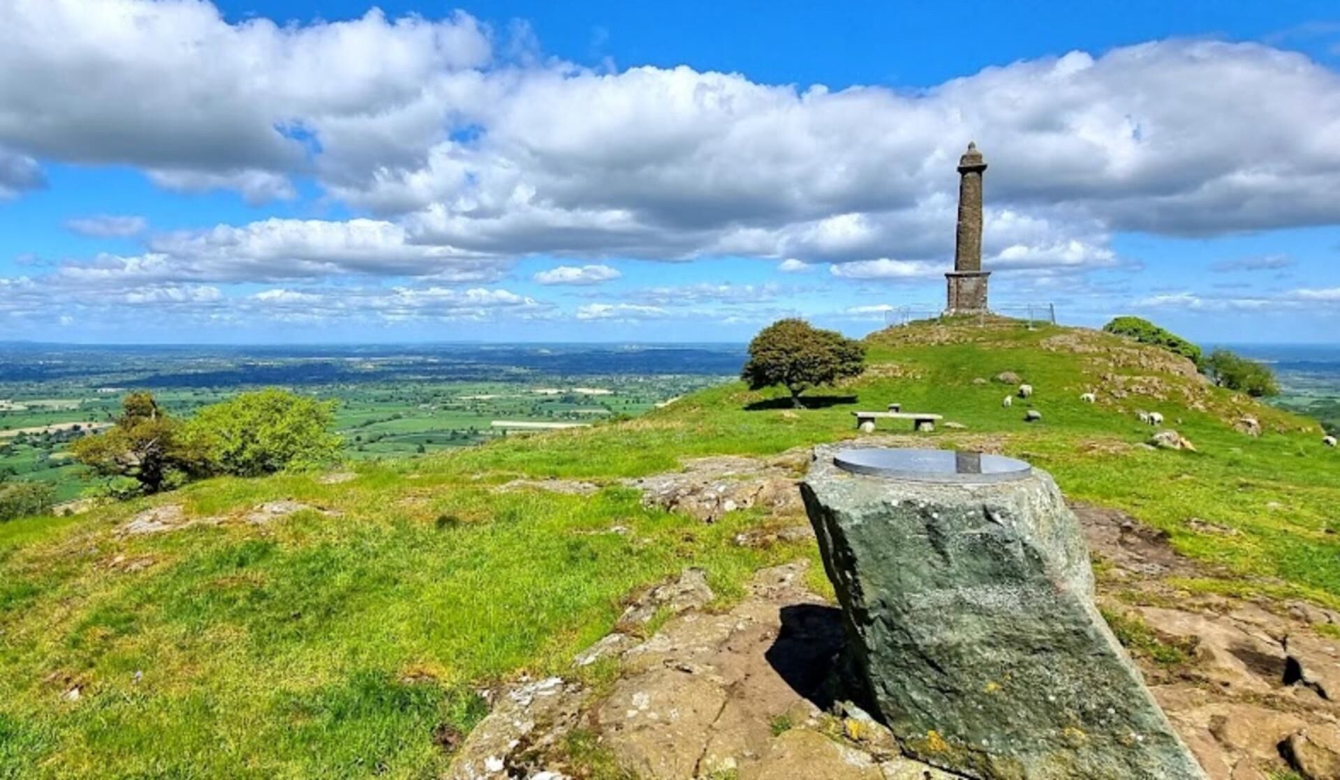 Un monumento in pietra su una collina erbosa con una vista panoramica del paesaggio circostante.