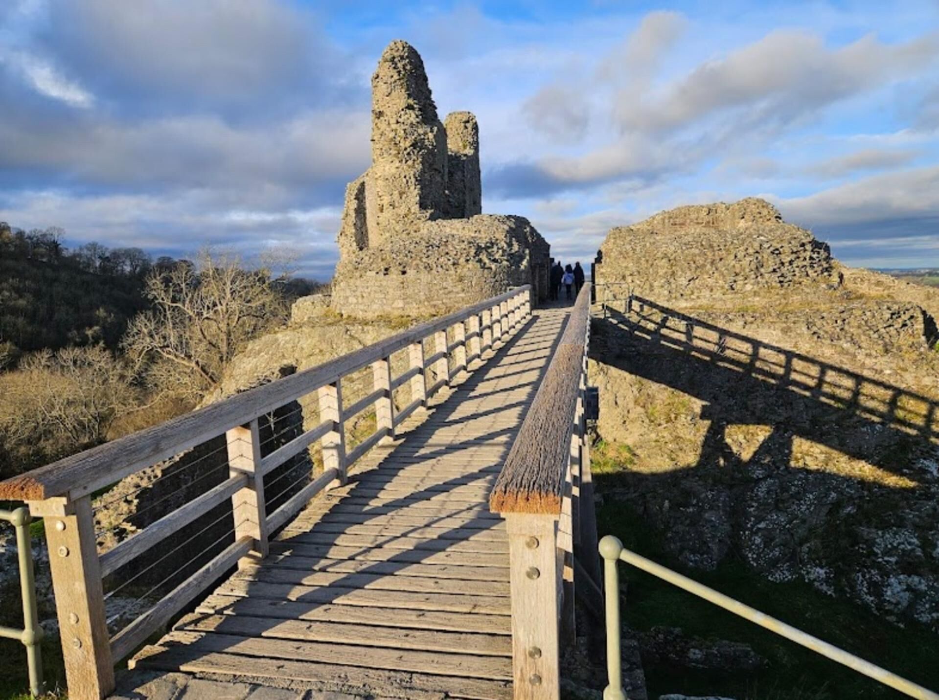 Pasarela de madera que conduce a ruinas de piedra antiguas bajo un cielo despejado.